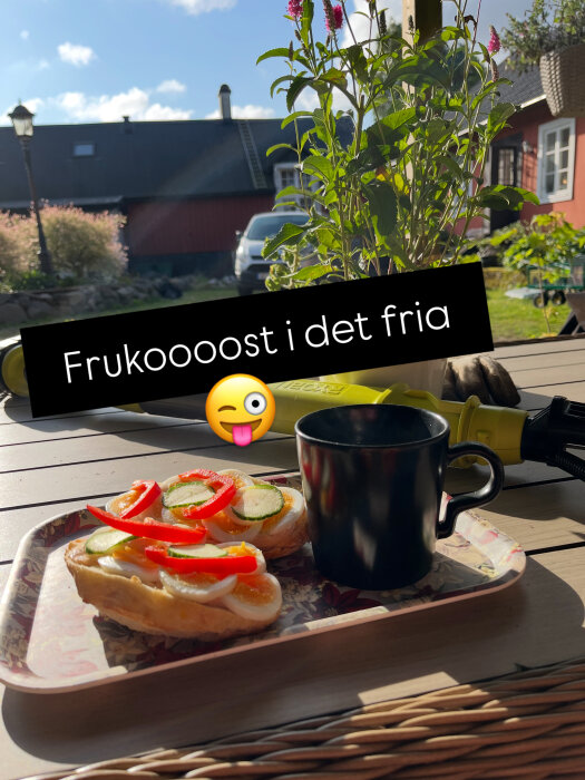 Äggmackor med paprika och gurka på ett fat och en kopp svart kaffe på en uteplats, omgiven av blommor och landskap.