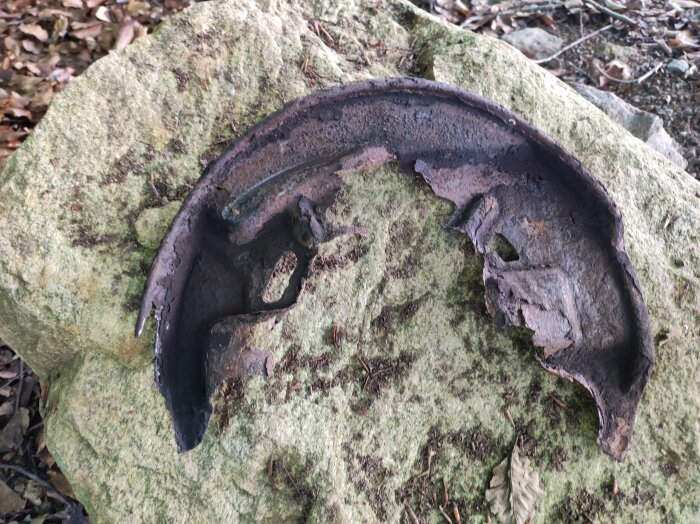 Rostig och trasig metallbit på en mossig sten i skogsmiljö.