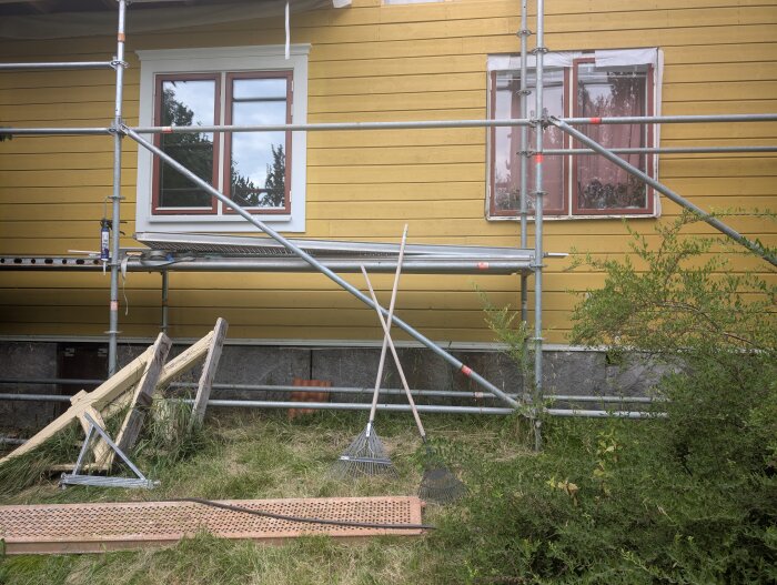 Fasad med två fönster, byggställning och verktyg i närheten. Ett fönster ska bytas ut innan semestern är slut.