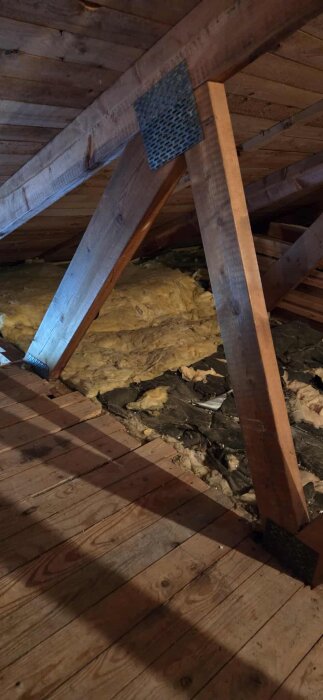 Närbild av takstol och träbalk under ett snedtak på en kallvind, med isolering synlig i bakgrunden.