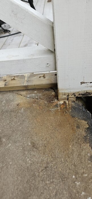 Sprickor i betonghörn under vitmålad stolpe på farstukvist. Betongen visar tecken på skador och fukt, med ojämna kanter och färgmissfärgningar.