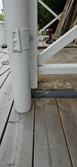 Vit stolpe på farstukvist placerad på träplanka ovanför sprucken murad matkällare. Verktyg synliga i bakgrunden.