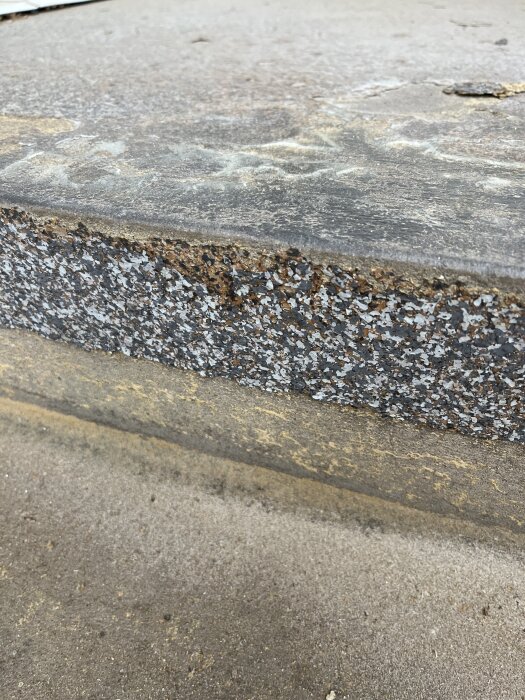Betongtrapp/platts belagd med grå flisliknande material som har börjat lossna, potentiellt halkskydd, fotograferad utomhus.