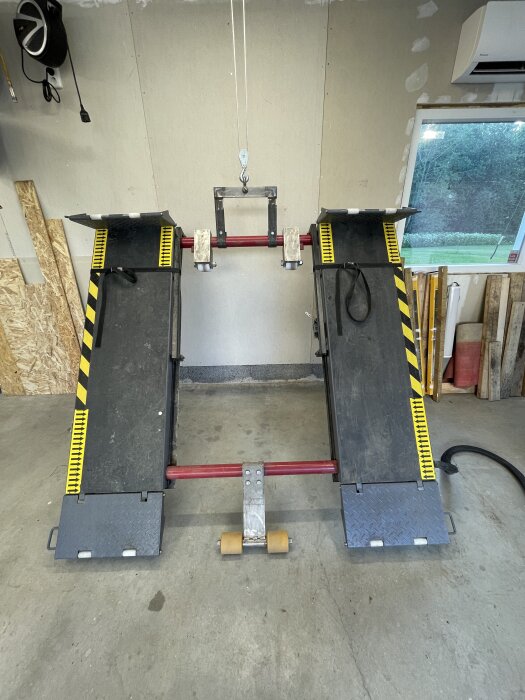 Portabel bilramp i ett garage med röd stång, härdsmält block och två uppkörningsramper med svart och gul striping.