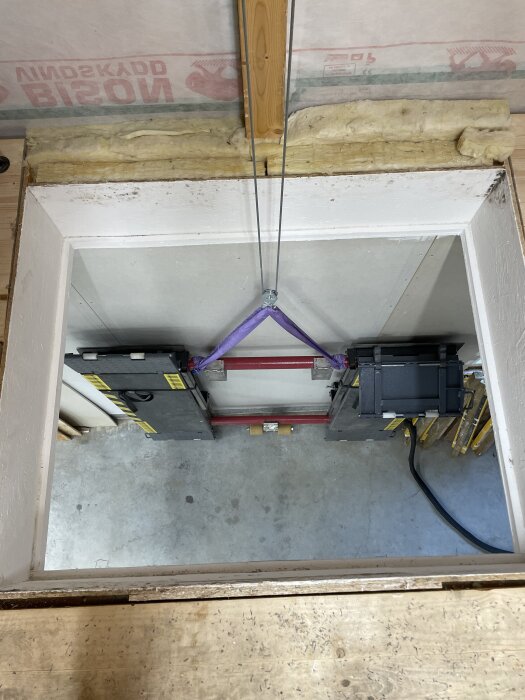 Byggkonstruktion av hissöppning sett ovanifrån, med trä- och metallkomponenter samt isolering runtom.