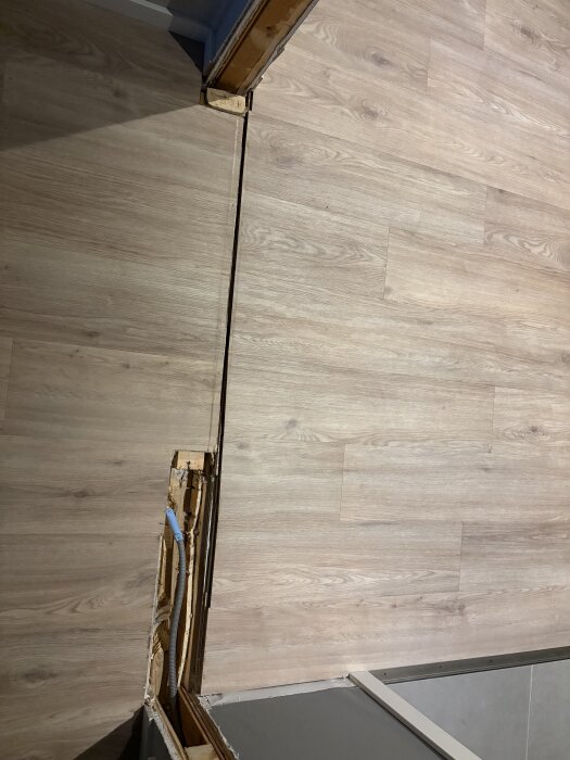 Öppning mellan rum med ljust trägolv, borttagen dörrpost och delar av vägg synliga, fråga om att jämna till ytan efter renovering.