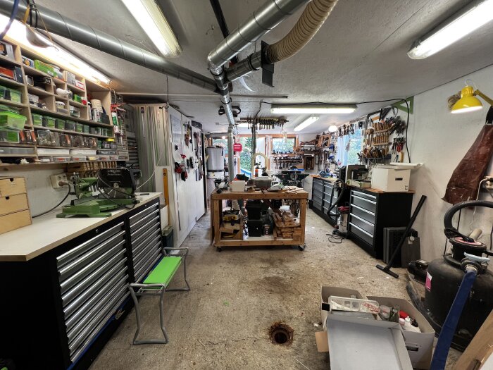 Verkstad med verktygsbänkar, hyllor fulla av förvaringsboxar och verktyg, samt arbetsbänkar och dammsugare, i en organiserad miljö.