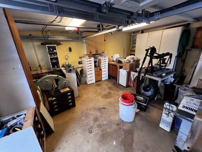 Verkstad med verktyg och utrustning, oorganiserat utrymme fullt med skåp, kartonger och maskiner, inklusive svarv och olika tillbehör.