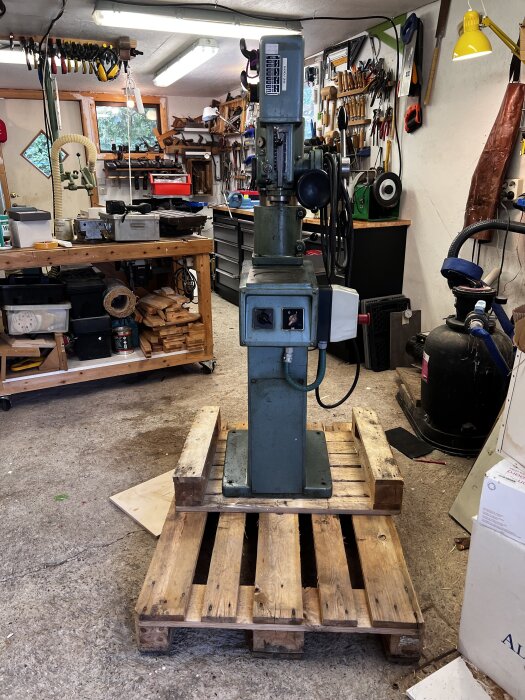 Maskin på lastpall i verkstad med verktyg, arbetsbänkar och utrustning runtomkring.