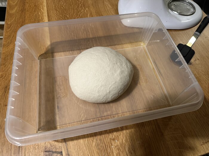 Degboll för pizza i en plastlåda på en träyta.