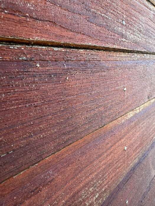 Närbild av en trävägg med rött träpanel, viss åldrande textur och spikhuvuden synliga i brädorna.