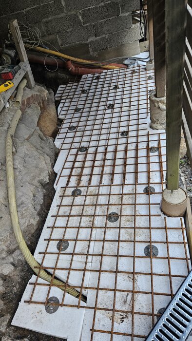 Armeringsjärn ovanpå 100 mm isoleringsskivor, förberett för gjutning av betong med tjocklek 50-60 mm, runtom omgiven av väggar och rör.