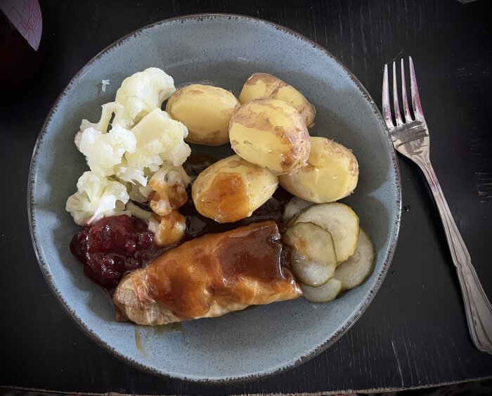 Tallrik med kåldolmar, kokt färskpotatis, kokt blomkål, lingon och inlagd gurka.