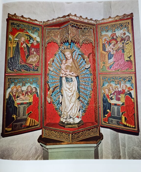 Religiös triptyk med skulptur av krönt kvinna och barn i centrum, omgiven av målade paneler med bibliska scener på sidorna.