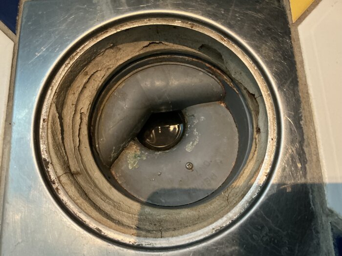 Golvbrunn i dusch med metallram, fastsatt med skruv. Tecken på slitage syns runt brunnen.