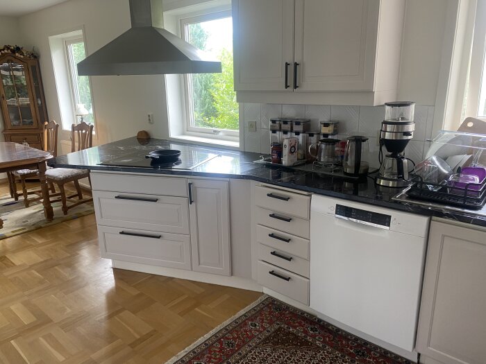 Kök med mörk bänkskiva, nedsänkt diskho, spishäll, diskmaskin och köksapparater. Bänkskivan täckt med plastfilm.