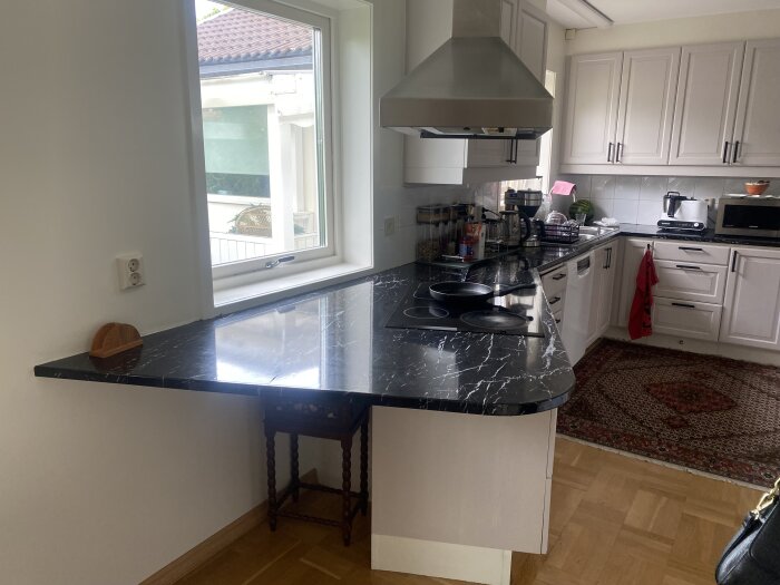 Kök med svart marmorerad bänkskiva, nedsänkt diskho och spis. Plastfilm över laminatet. Inte standardmått. Vit skåpinredning.