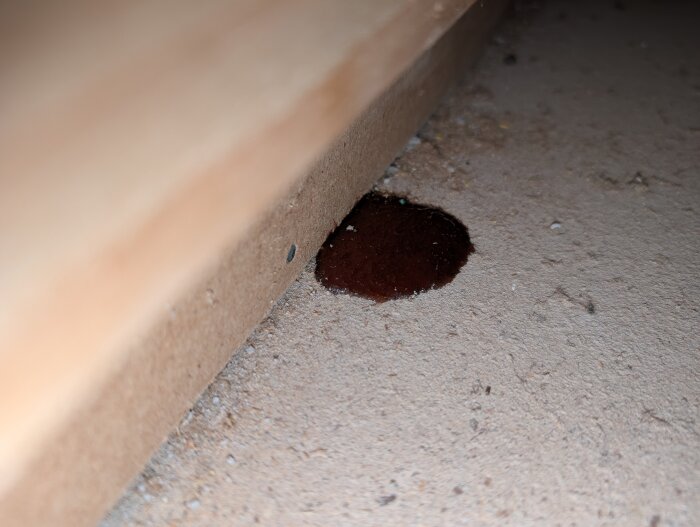 Mörk fläck på golvspån, liknande halvtorkad sirap, under ett köksskåp i trähus från 1983.