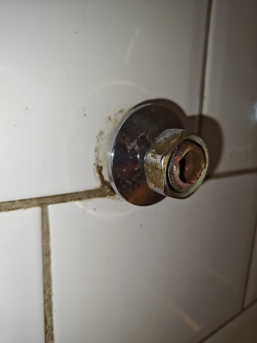 Väggmonterad köksblandarfästning i vit kakelvägg, delvis demonterad.