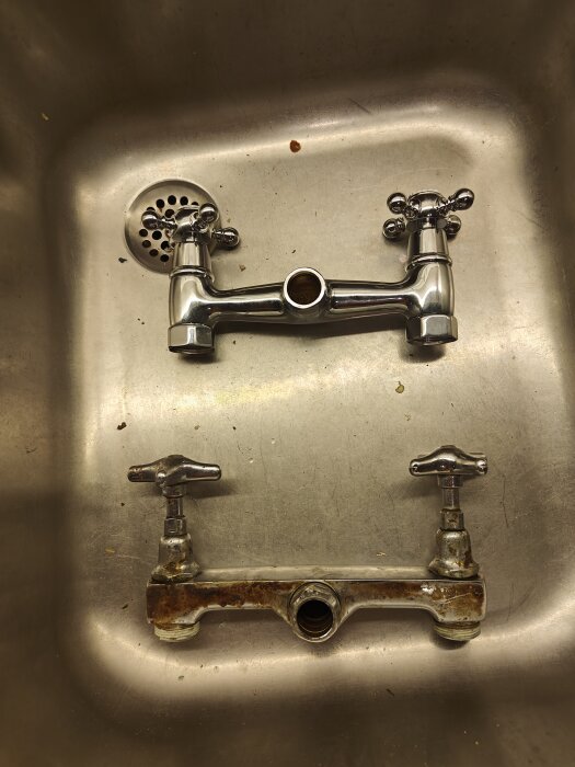 Två olika kranar placerade i en diskho, den nya kromade är smalare än den gamla rostiga.