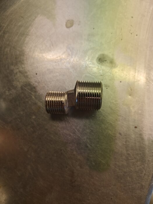 Metalladaptern för rörkopplingar ligger på en yta, använd för justering vid bygg- eller renoveringsprojekt.