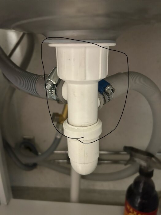 Vit plastdel avloppsuttag med inkopplad slang under diskbänk, ringad i bild, ofta använd vid tvättmaskinsinstallationer.