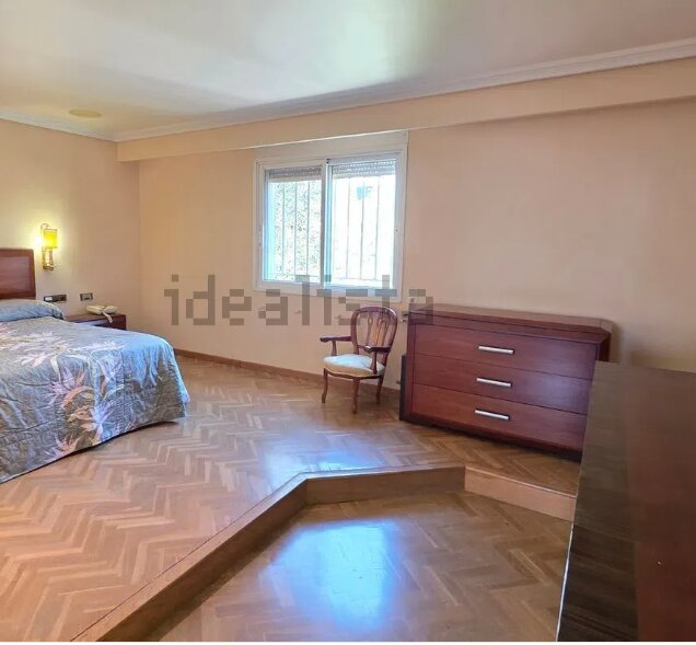 Sovrum med en plattform i mitten av golvet, en säng till vänster, en byrå och stol vid fönstret. Plattformen skapar höjdskillnad i rummet.