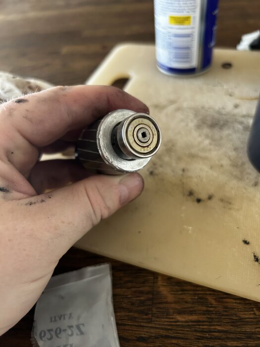 Närbild på en hand som håller en rotormotor med ett fastsittande lager, omgiven av oljiga verktyg och en sprayburk i bakgrunden.