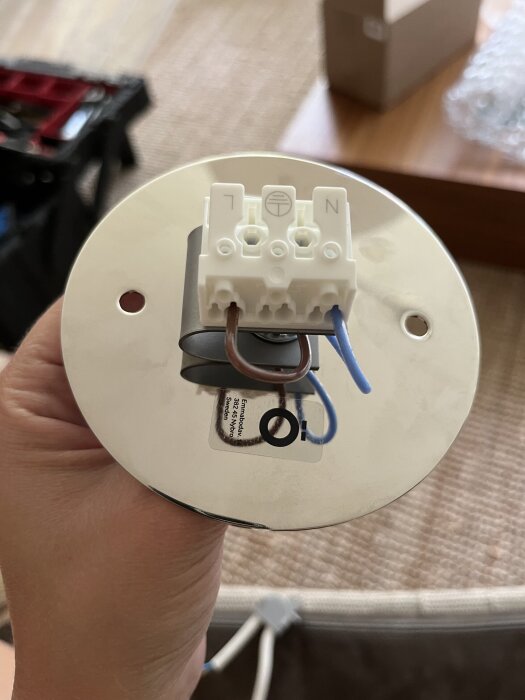 Hand holding a lamp connector showing brown and blue wires inserted into the right ports of a white terminal block, with Örsjö sticker visible.