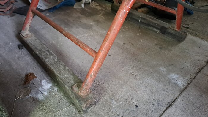 Metallsargen av en slipmaskin utan hjul, med två trämedar som bas, på ett smutsigt cementgolv.