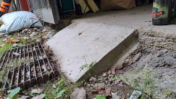 Betongramp vid utfart med galler till vänster. Omgiven av höstlöv och gräs, delvis skuggad under laduutbyggnad.