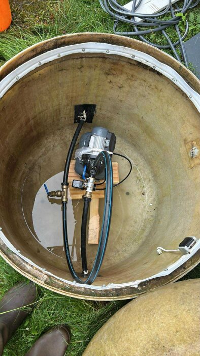 Glasfiberbrunn med vatten, motor och slangar samt synliga hål i botten.