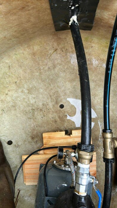 Hål i botten av glasfiberbrunn med rör och kopplingar synliga mot en betongliknande yta.