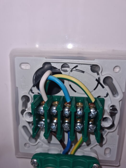 Elinstallation med kablar och kopplingsplint synliga i en väggdosa i ett badrum, med gröna, blå och vita kablar anslutna.