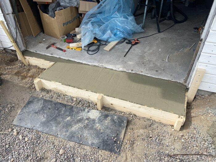 Nybyggt betongtrappsteg vid garageingång med verktyg och material runtom, del av pågående renovering.