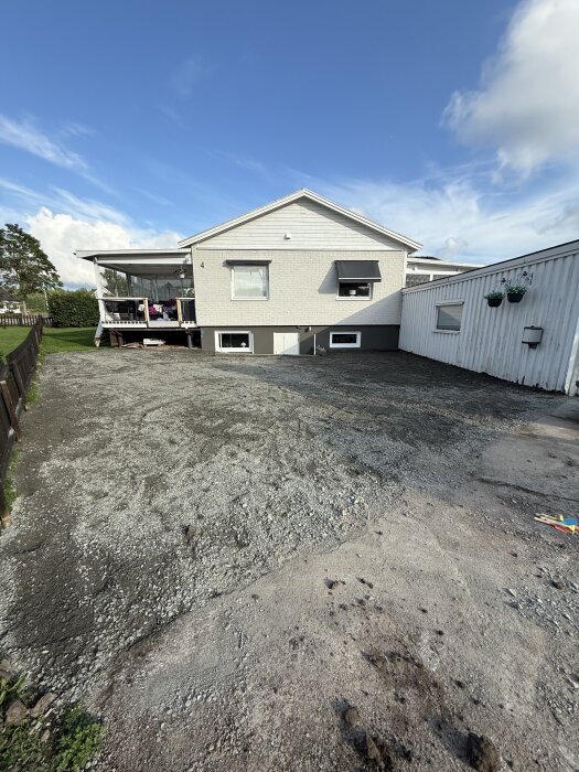 Grusad uppfart framför ett vitmålat hus med markplaneringsprojekt pågående, blå himmel i bakgrunden.