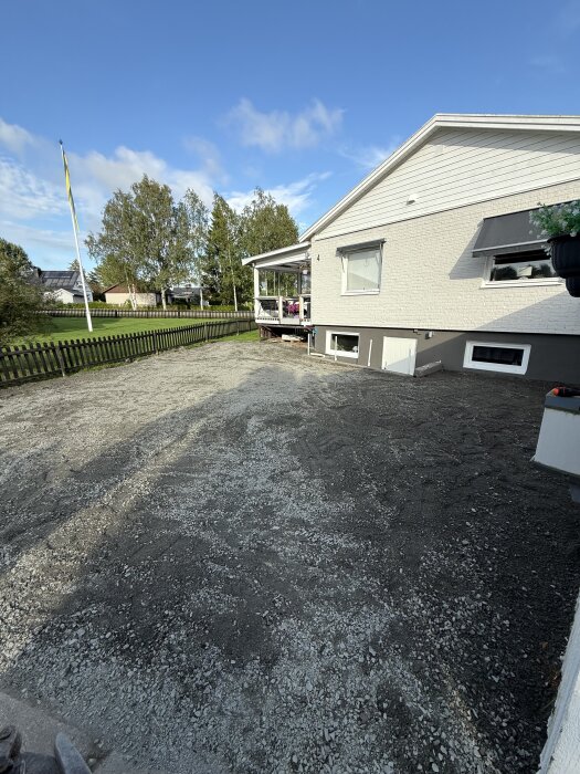 Grusyta förbereds som uppfart vid ett vitmålat hus med veranda.