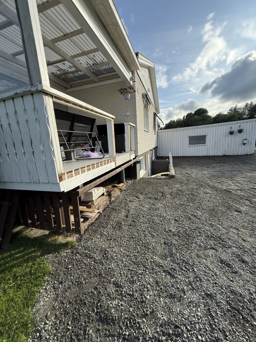 Uppfart med nyanlagt bärlager av grus, intill hus med veranda och trappa, solig dag med delvis molnig himmel.