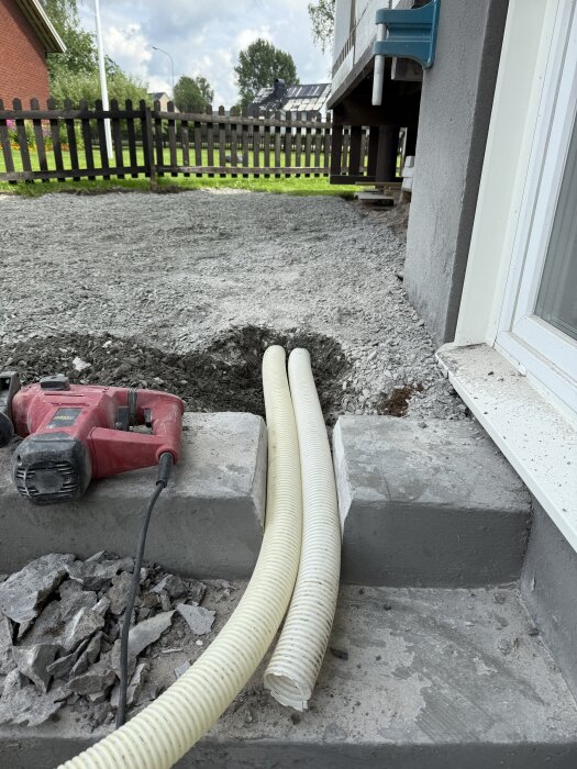 Två avloppsrör lagda på en källartrappa av betong, omgivna av grus och byggverktyg.