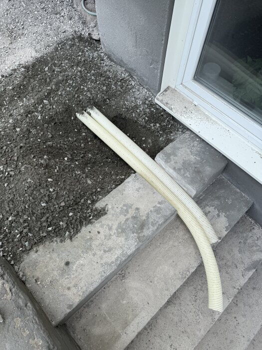 Dräneringsslang placerad på stenlagda trappsteg bredvid grusfyllning närmast husvägg.
