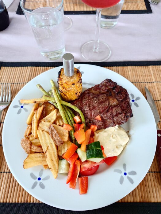 Tallrik med entrecote, pommes chips, grillad majs, sparris och sallad.