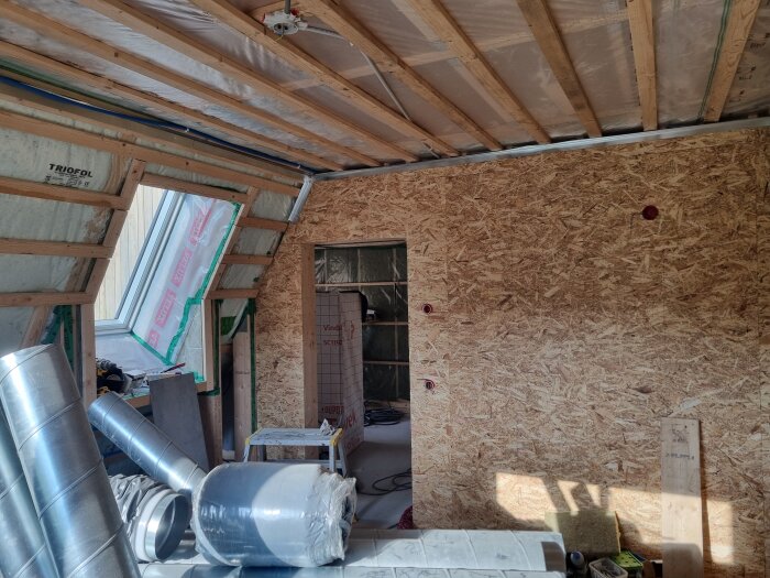 Renovering av sovrum med OSB-skivor på väggarna och gipsskivor i taket, verktyg och material ligger utspridda på golvet.