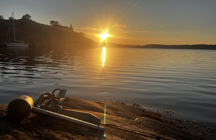 Solnedgång över vatten i skärgården, verktyg på klippa i förgrunden.