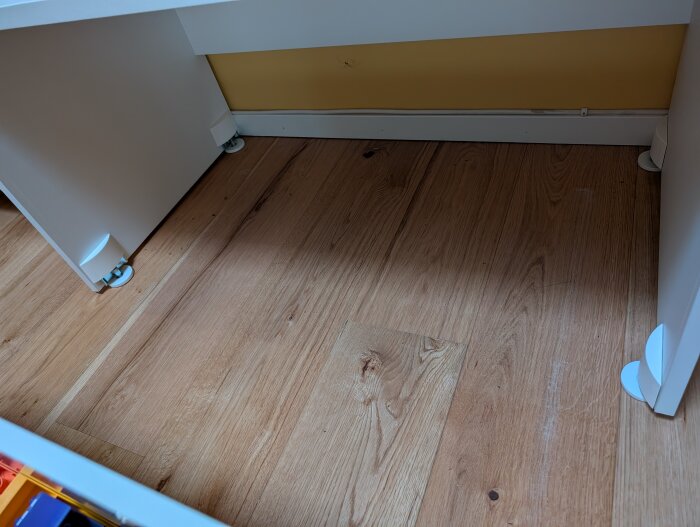 Golvet visar märken och repor från två bänkar med förvaring som glider snett. Ljus träyta med symmetriska slitageområden nära väggarna.