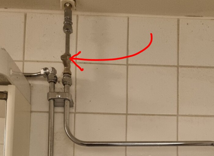 En röd markering visar en ventil på ett rörsystem för en handdukstork monterad på kakelvägg i ett badrum.