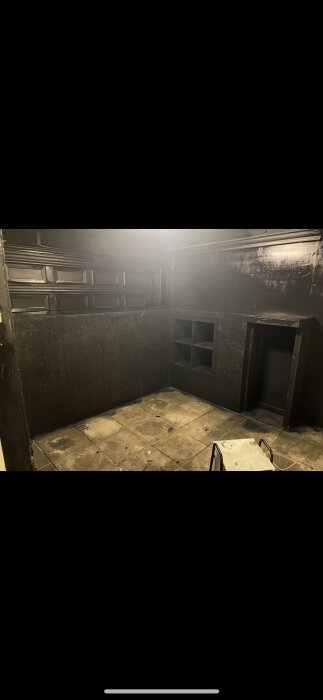 Svart interiör i ett ombyggt garage med isolerade väggar, marksten på golvet och hyllor längs väggen.