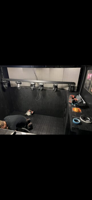 Person arbetar i ett svartmålat garage med flera kameror monterade längs väggen. Verktyg och kablar ligger på en bänk.