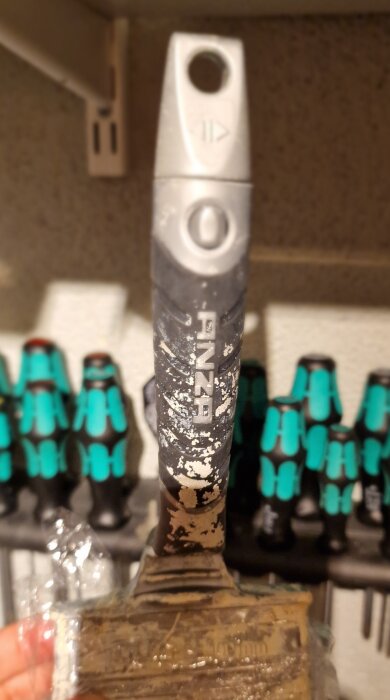 Anza 100mm pensel med använd färg och tydliga detaljer på handtaget syns, inklusive pilar på toppen framför verktyg i bakgrunden.