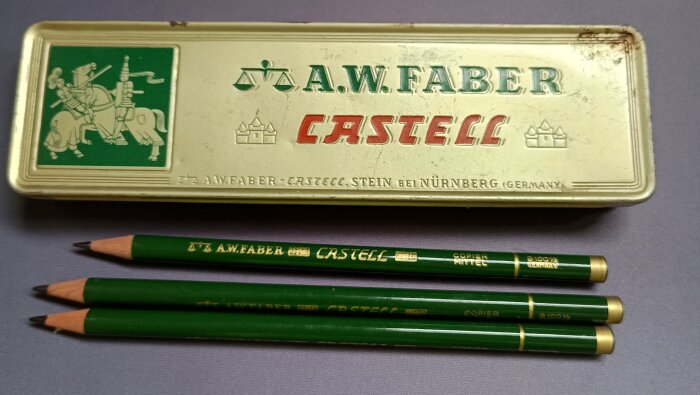 Plåtask med texten "A.W. Faber Castell" och tre gröna anilinpennor ligger framför.