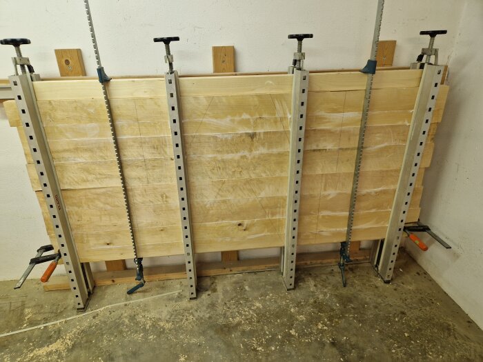 Björkplankor i en limpress i källaren för tillverkning av ett köksbord. Fyra tvingar håller ihop plankorna i pressen.